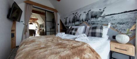A bedroom with a large bed, a television mounted on the wall, and a mural of sheep on the wall.
