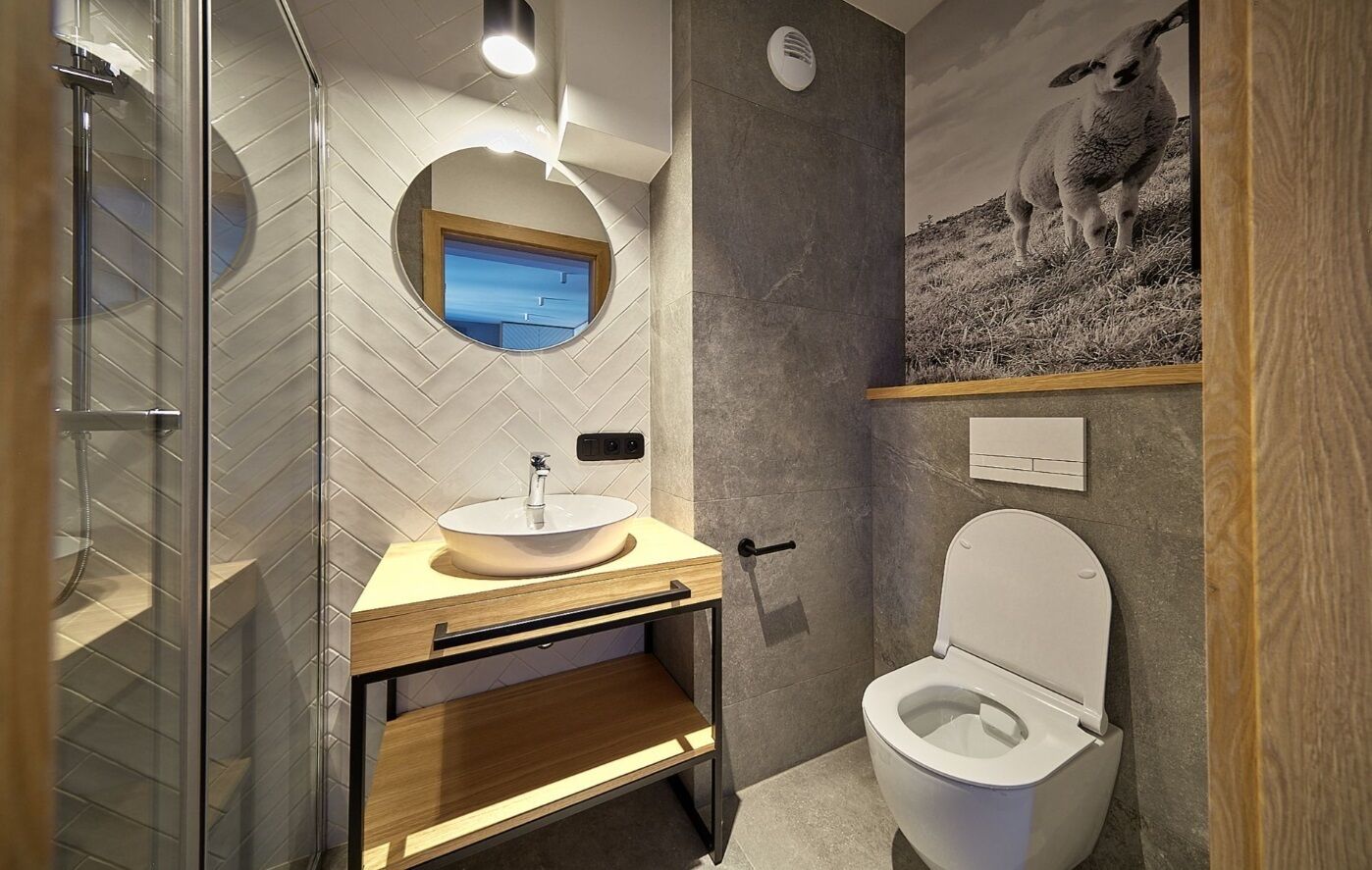 Moderni kylpyhuone, jossa on lasinen suihkuseinä, puinen allaskaappi ja wc.
