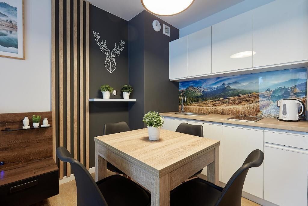 A modern kitchen with white cabinets, a wooden dining table, and a large window with a scenic view.