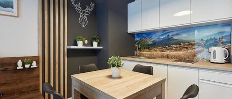 A modern kitchen with white cabinets, a wooden dining table, and a large window with a scenic view.