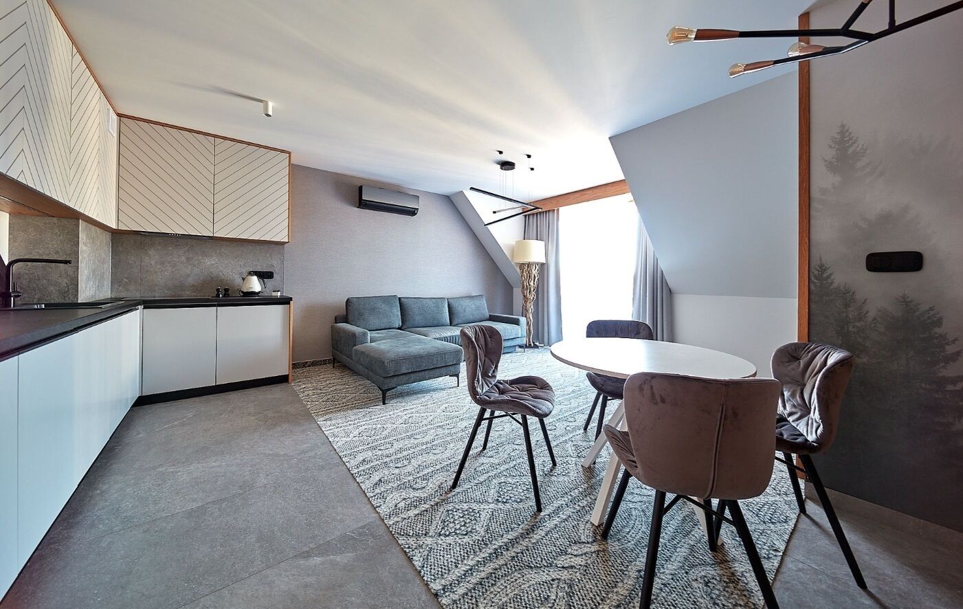 A modern kitchen with a built-in stove, a grey sofa, and a dining area with a round table and chairs.