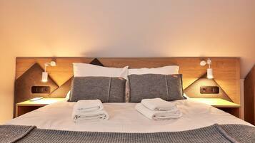 A neatly made bed with pillows and folded towels, a wooden headboard, and bedside lamps.