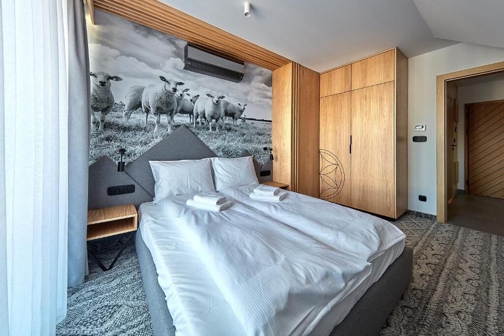 Una camera da letto moderna con un letto grande, un'armadio in legno e un murale con pecore sulla parete.