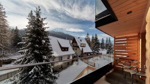 Une cabane moderne en bois dotée d’un balcon en verre qui offre une vue sur un paysage enneigé et un village.