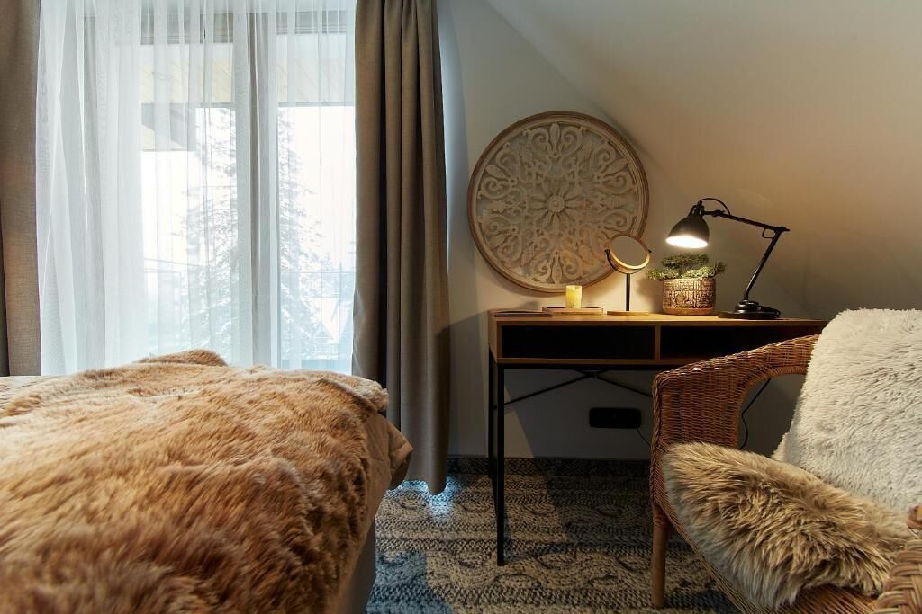 A hotel room with two beds, a desk with a lamp, a decorative wall piece, and a view of the outdoors.