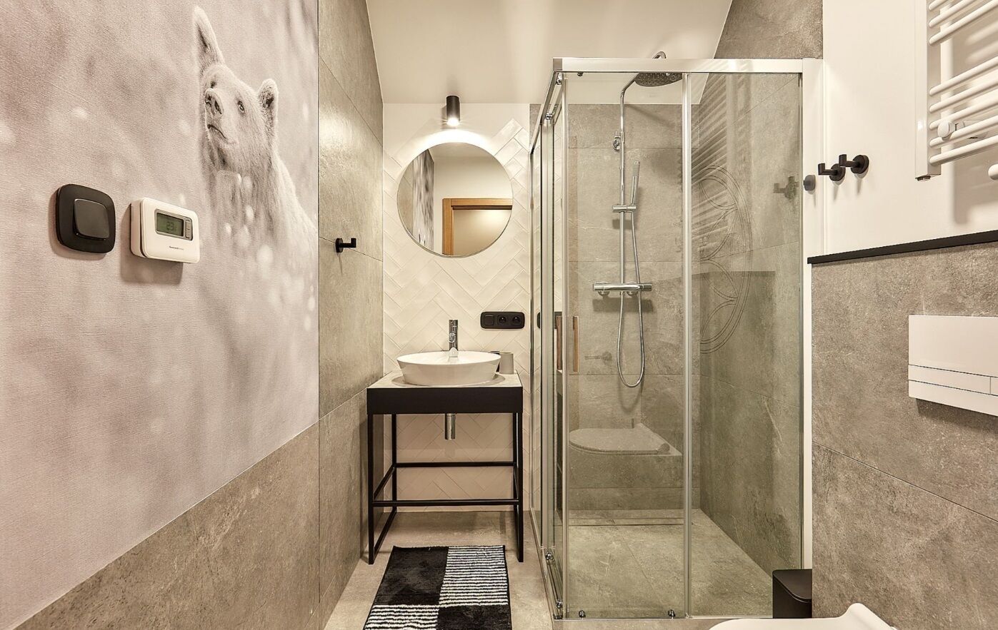 A modern bathroom with a glass shower enclosure, a sink with a mirror, and a wall-mounted thermostat.