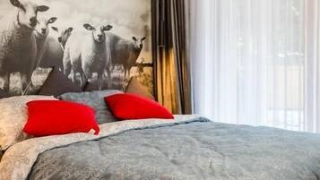 Un dormitorio con una cama grande, un mural de ovejas en la pared y cortinas translúcidas en la ventana.