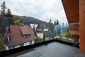 A balcony with a view of houses and a forested hill. - Tatra Square Apartments (Zakopane)