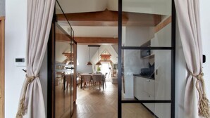 Une cuisine moderne avec des poutres en bois, un coin repas doté d’un parquet en chevrons et une vue sur l’espace de vie.