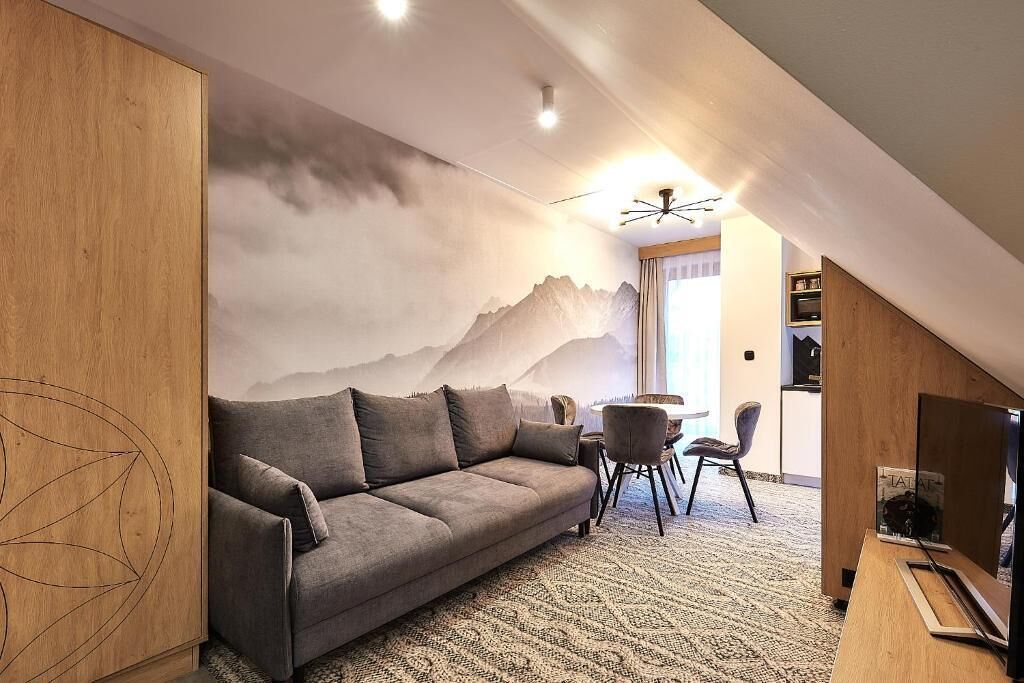 Ein modernes Wohnzimmer mit grauem Sofa, einem Esstisch mit Stühlen und einer Wandmalerei mit Bergmotiv.