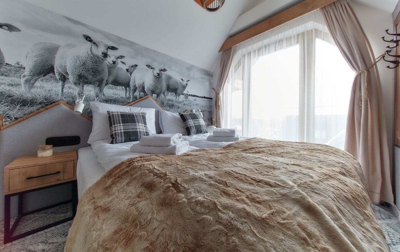 A bedroom with a large bed, a nightstand, a wall-mounted shelf, and a window with curtains.