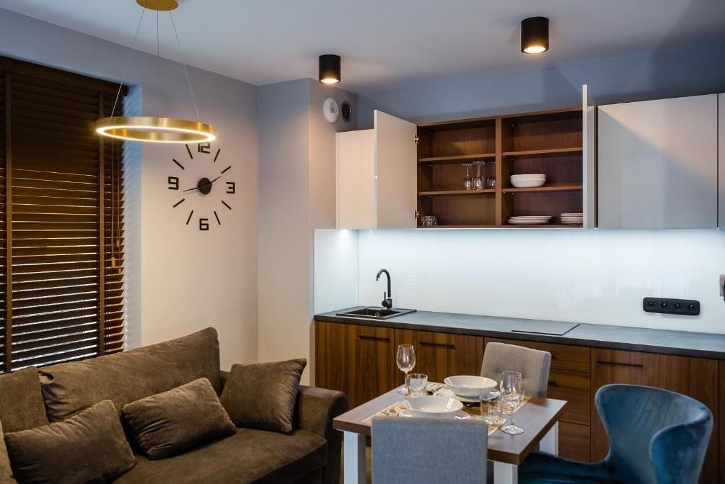 Eine kompakte Küche mit eingebauter Uhr, Holzschränken und einem Essbereich mit Tisch für zwei Personen.