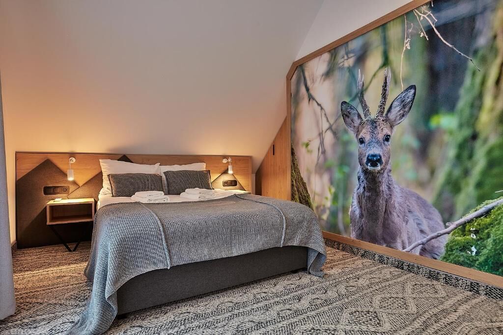 Een slaapkamer met een groot bed, een nachtkastje, een wandlamp en een groot schilderij van een hert op de muur.