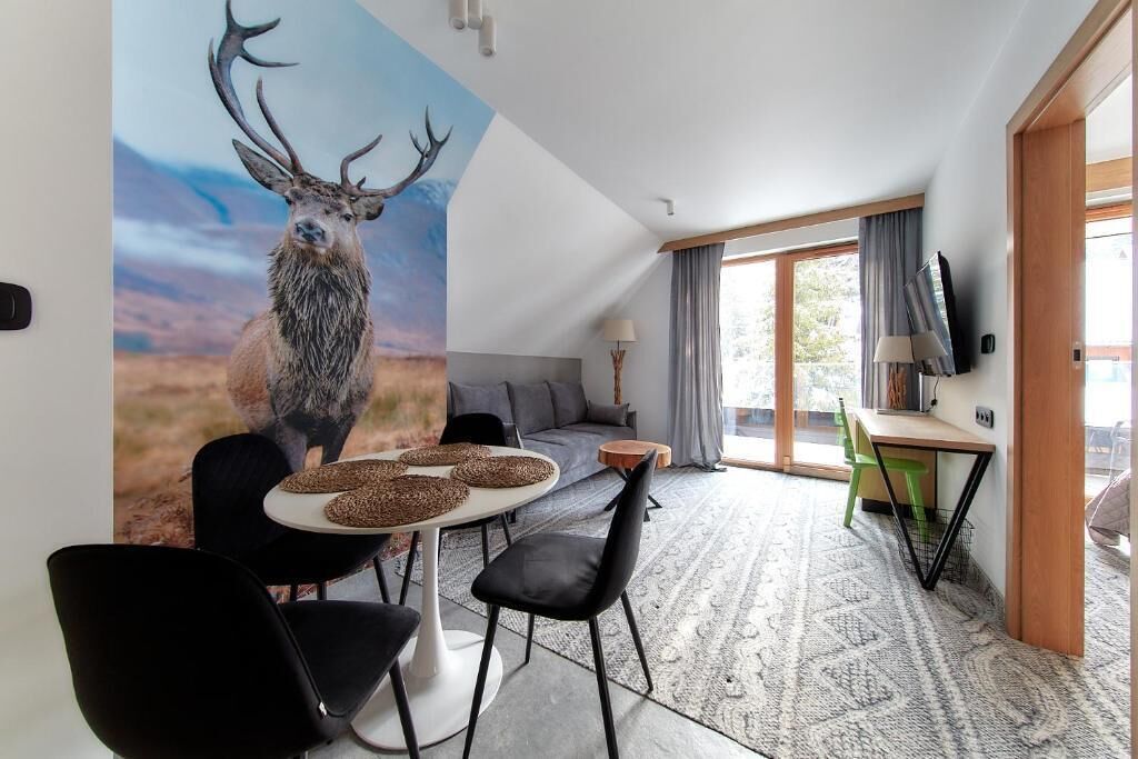 A modern living room with a large deer painting, a dining area with a round table and chairs, and a TV mounted on the wall.