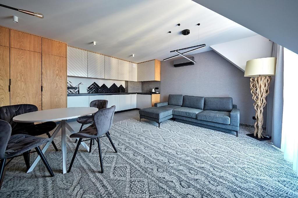 A modern living room with a grey sofa, a round coffee table, and a dining area with chairs.