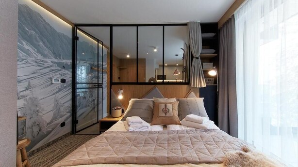 Une chambre d’hôtel moderne dotée d’un grand lit, d’une porte coulissante donnant accès à la salle de bain et offrant une vue sur le paysage urbain.