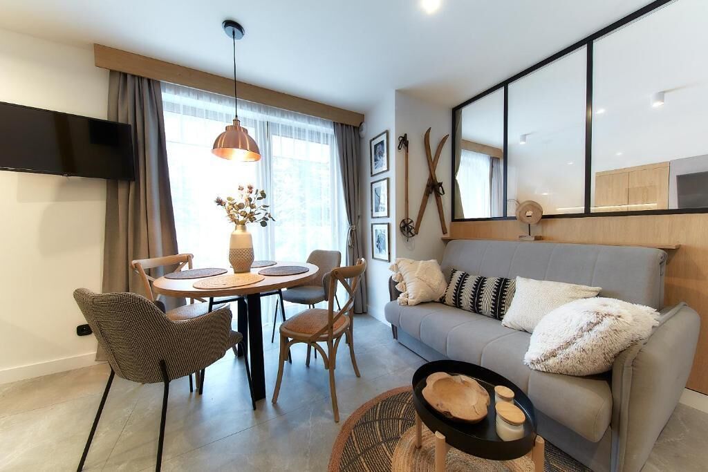 A modern living room with a sofa, dining table, chairs, and a TV mounted on the wall.