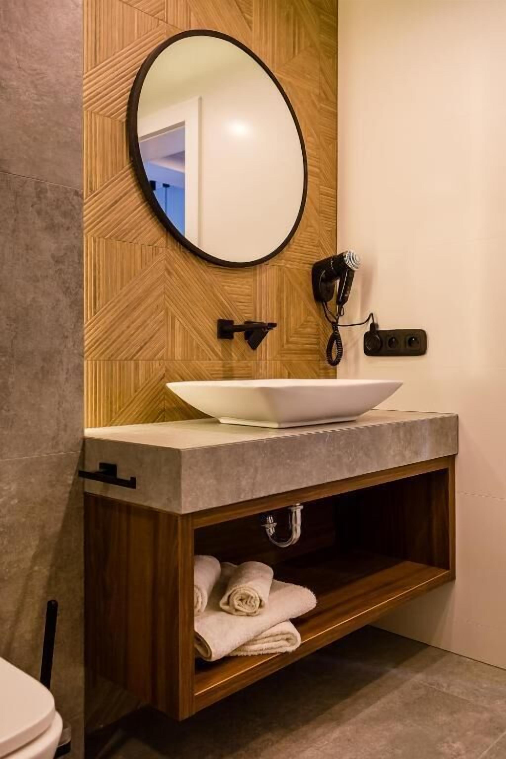 A modern bathroom with a wooden vanity, a round mirror, and a built-in towel rack.