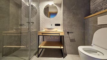 Et moderne badeværelse med en glasbrusekabine, en trækommode med vask og et toilet.