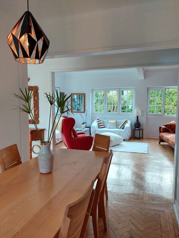 A spacious living area with a wooden dining table, red chairs, and a modern pendant light.