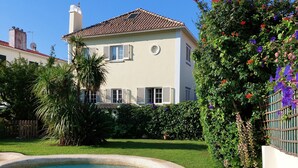 Una piscina con lettini, una casa con tetto in tegole e un giardino curato.