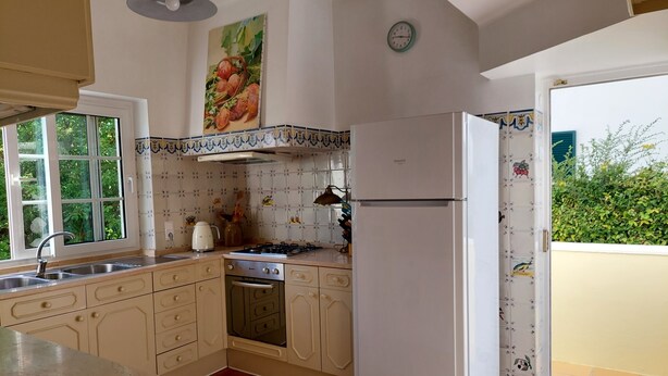 A kitchen with a gas stove, sink, and a white refrigerator. There is a window with a view of greenery outside. - Traditional Villa  with pool and garden 15 minutes walk to sea front & beaches.  (Cascais)