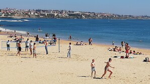 A beach with people playing volleyball, a sandy shore, and a cityscape in the background. - Traditional Villa  with pool and garden 15 minutes walk to sea front & beaches.  (Cascais)