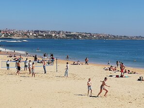 A beach with people playing volleyball, a sandy shore, and a cityscape in the background.