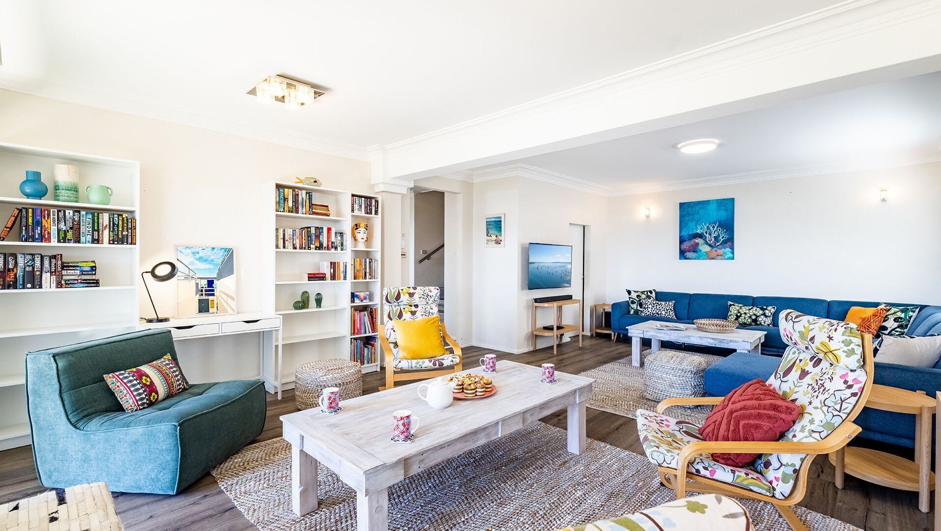 Una sala de estar moderna con un sofá azul, un sillón verde, una mesa de centro de madera y una estantería llena de libros.