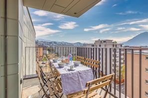 A balcony with a table set for dining, overlooking a cityscape with buildings and a mountain.