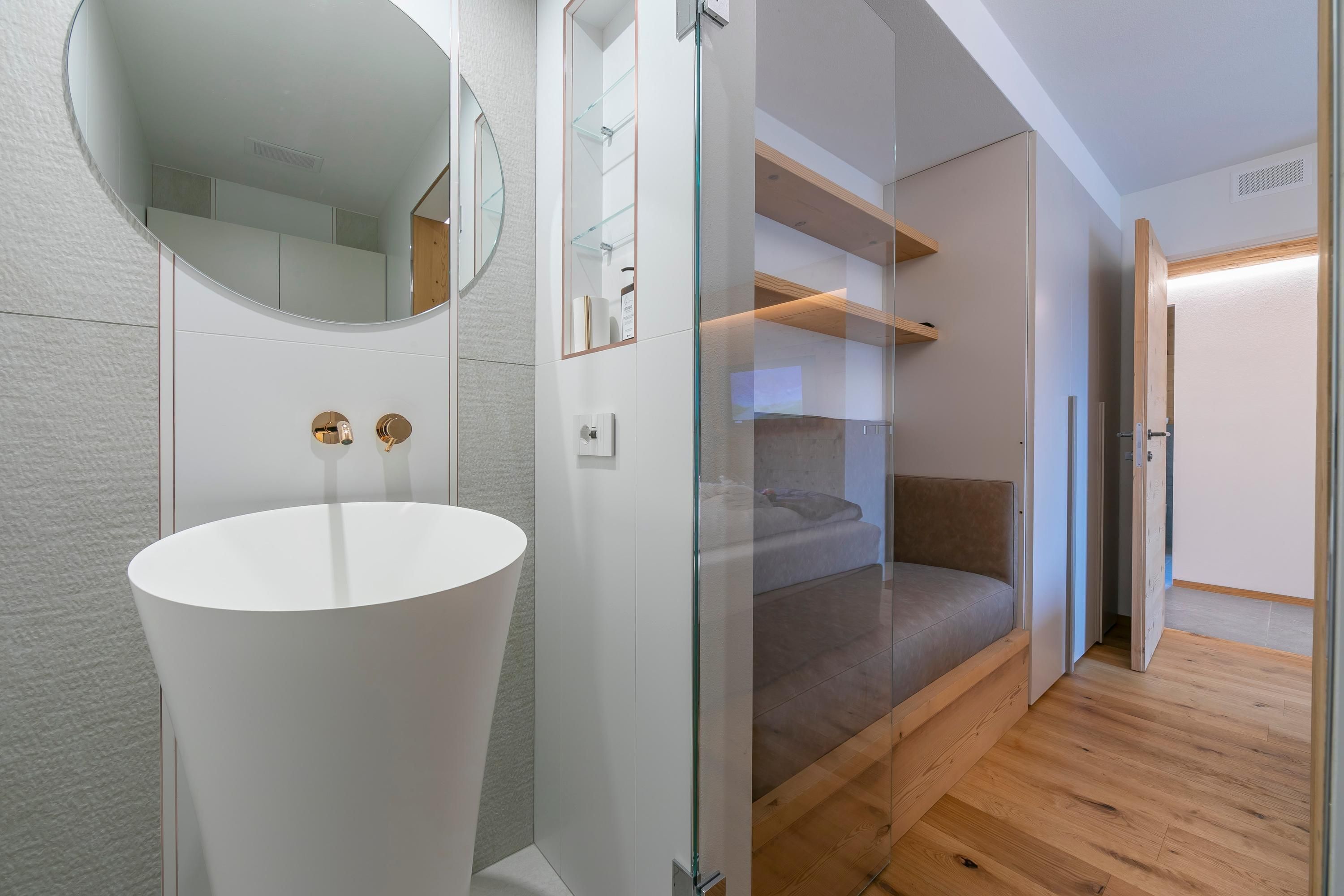 A modern bathroom with a white sink, a round mirror, and a glass shower enclosure.