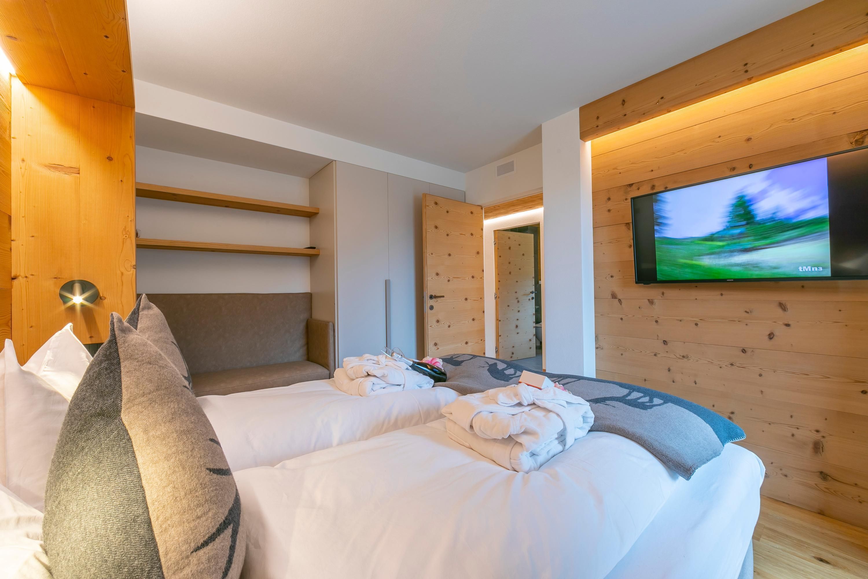 A hotel room with two beds, a flat-screen TV mounted on the wall, wooden paneling, and a view of the outdoors.