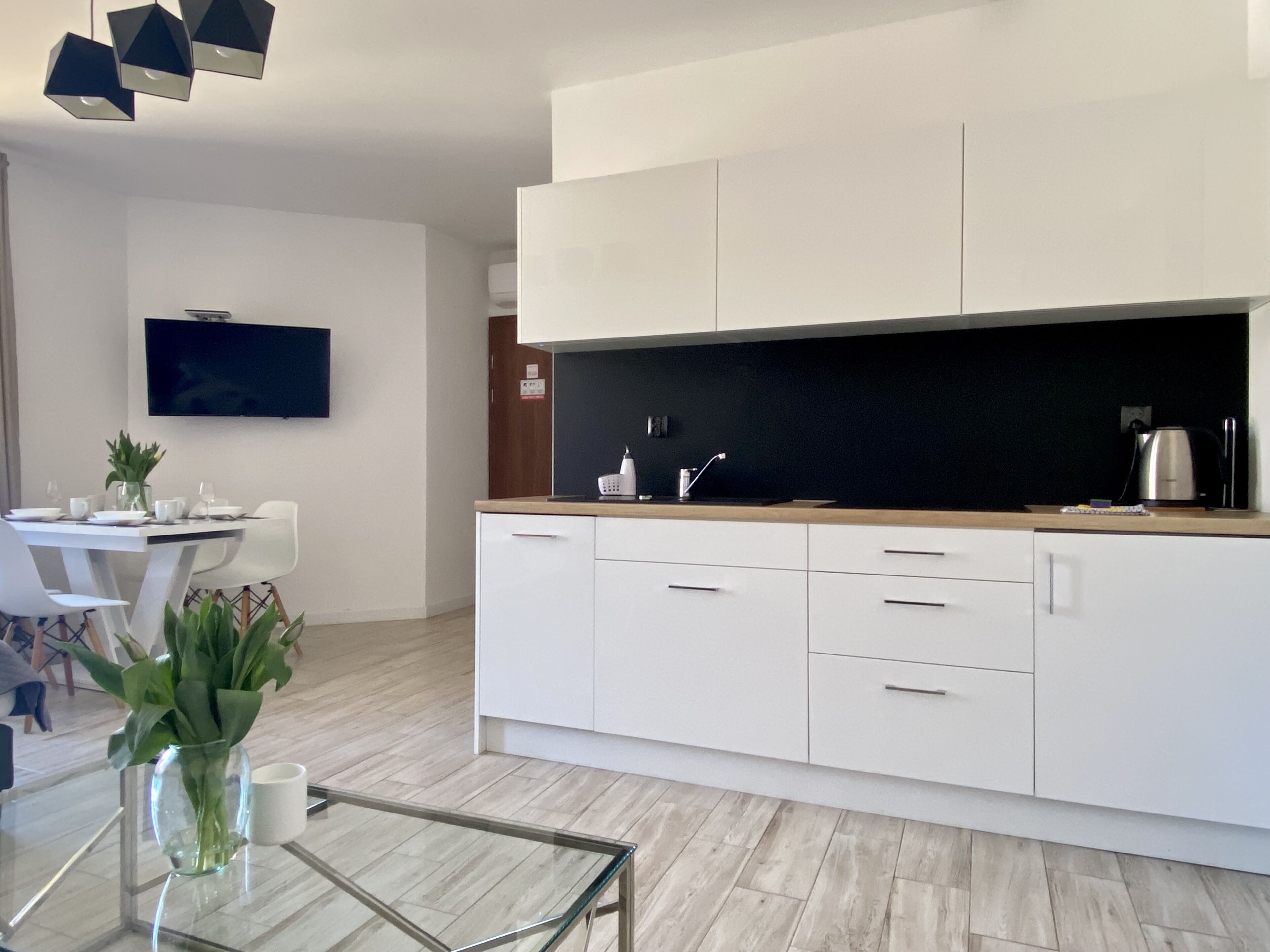A modern kitchen with white cabinets, a black countertop, and a glass coffee table.