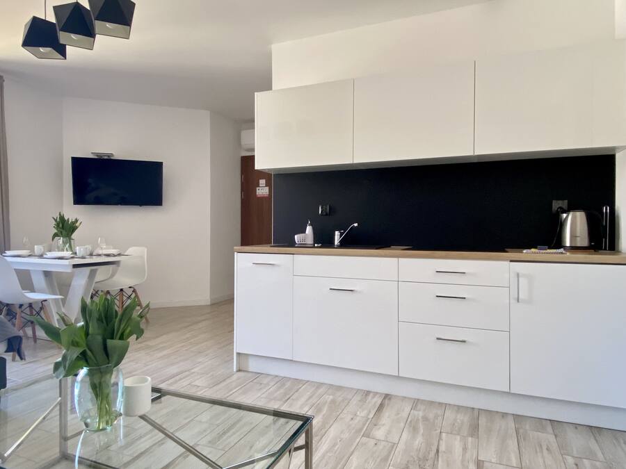 A modern kitchen with white cabinets, a black countertop, and a glass coffee table.
