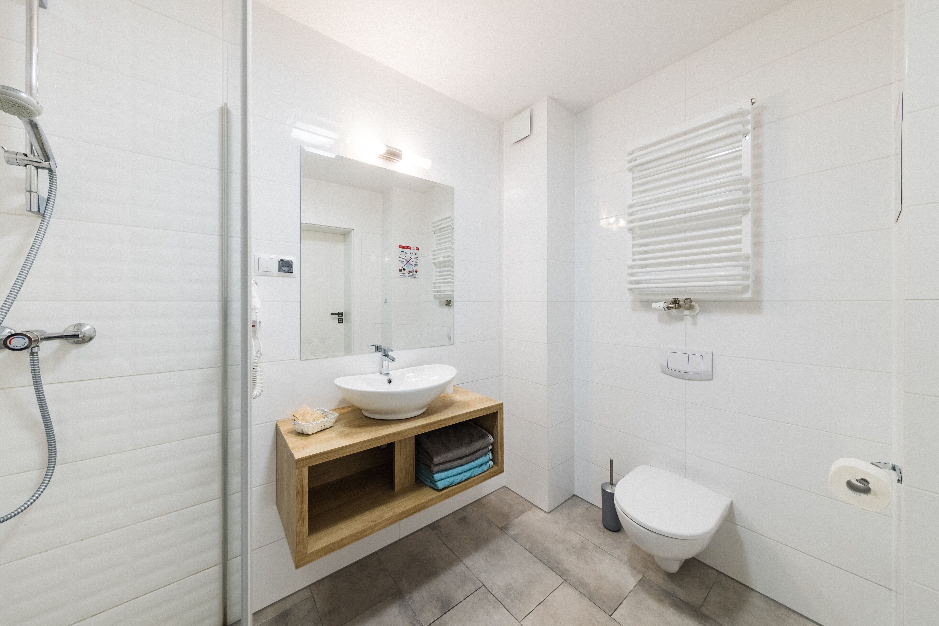 A modern bathroom with a glass-enclosed shower, a white sink with a wooden vanity, a toilet, and a radiator.