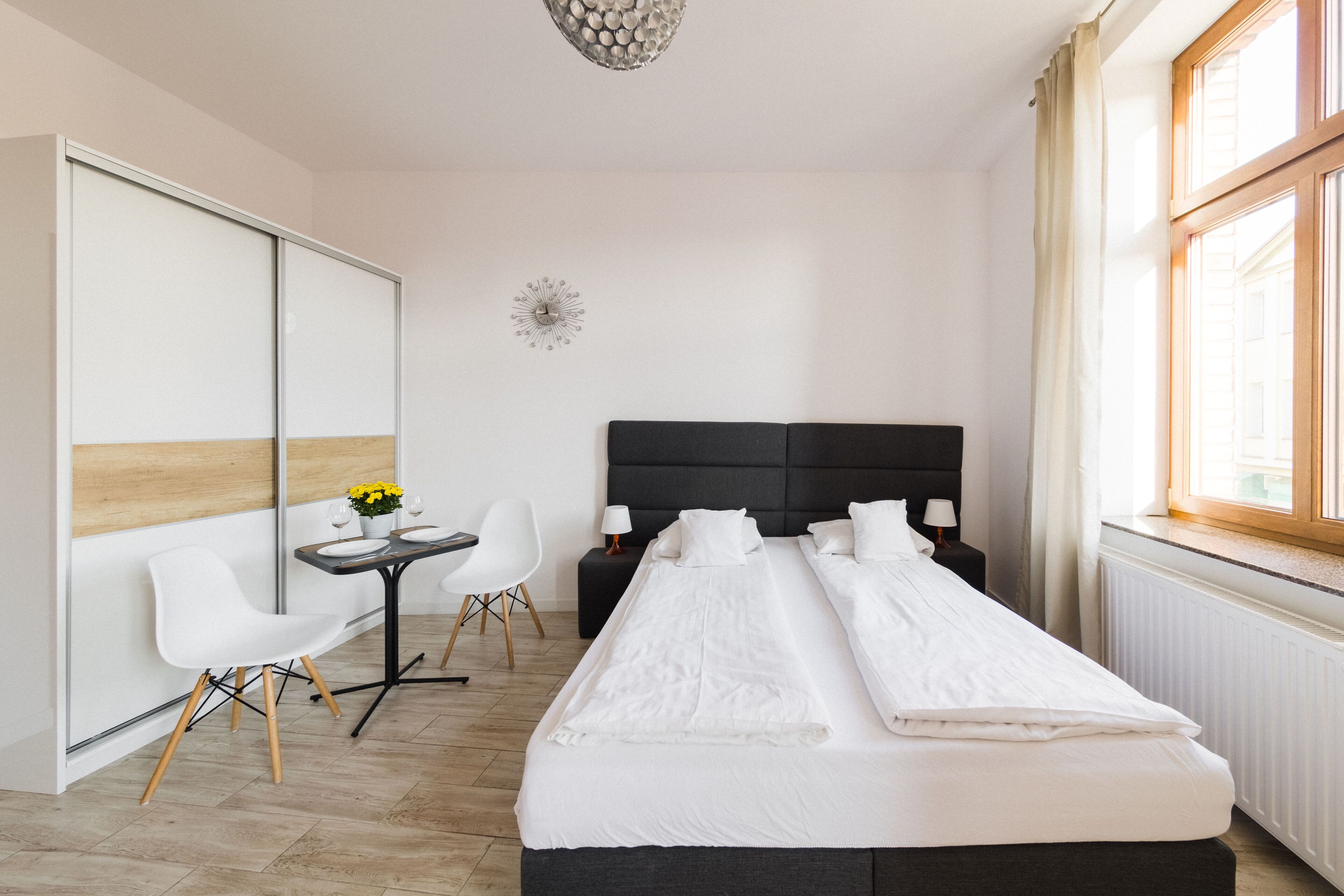 Habitación de hotel con cama, escritorio y sillas, una mesita con flores y una ventana con cortinas.