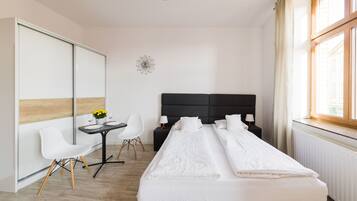 Habitación de hotel con cama, escritorio y sillas, una mesita con flores y una ventana con cortinas.