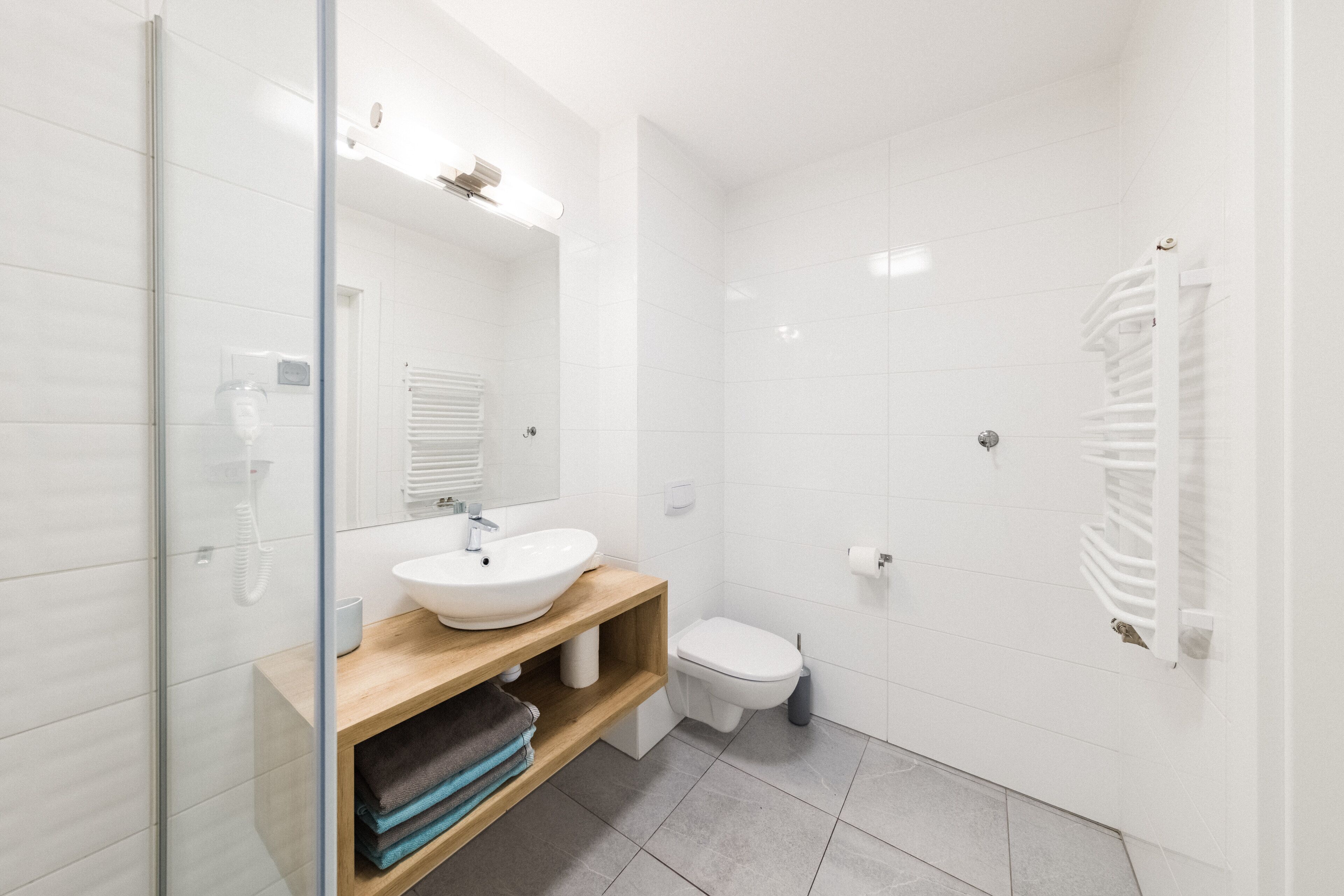 Une salle de bain moderne avec une douche à parois de verre, un meuble-lavabo en bois avec un lavabo blanc et des toilettes blanches.