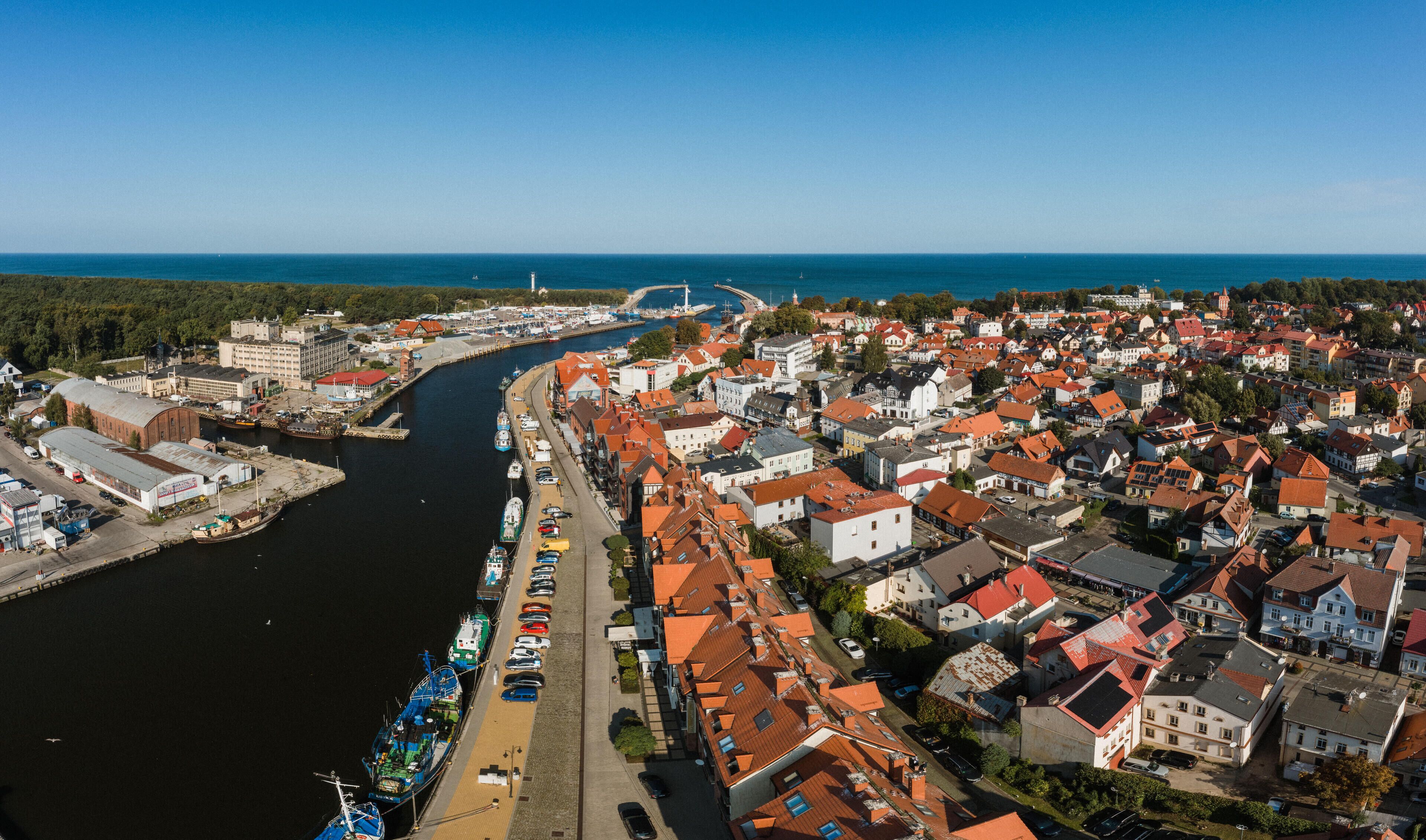 Vista aérea de uma vila costeira com um rio, barcos e uma ponte.