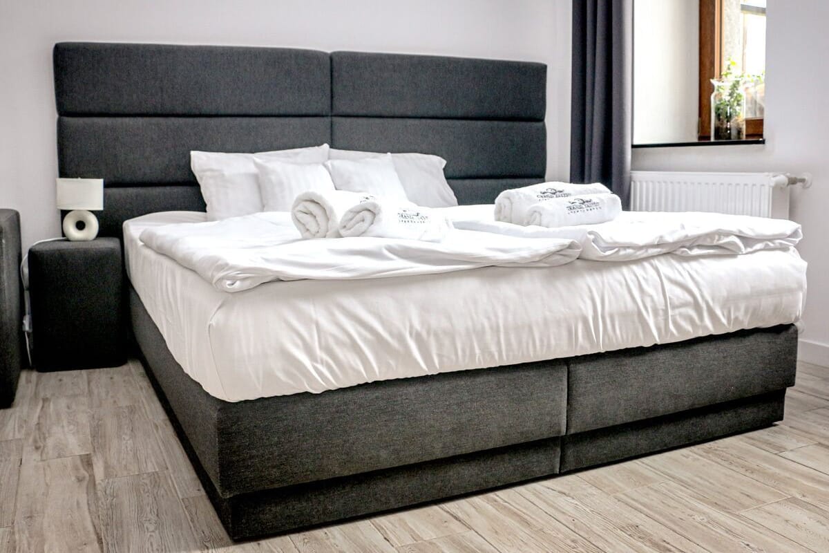 A modern bed with a grey headboard, white bedding, and neatly folded towels.
