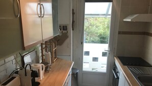 Cocina compacta con encimera de madera, un fregadero y una estufa. Se ve vegetación a través de la ventana.