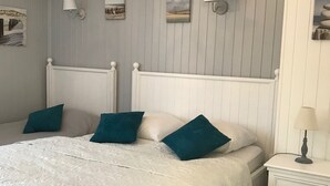 Una cama bien hecha con ropa blanca y almohadones verde agua, una mesita de noche blanca con lámpara, y un aplique de pared.