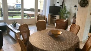 Un comedor con una mesa redonda, sillas de mimbre, un televisor y una planta en maceta.