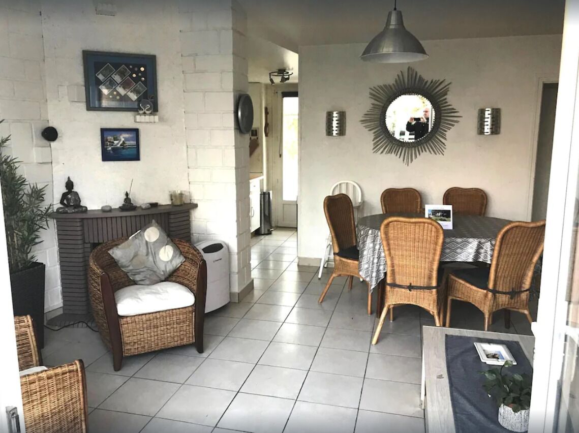 A dining area with wicker chairs and a table, a wicker sofa with cushions, and a mirror on the wall.