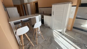 Una cocina con encimera blanca, dos taburetes de bar blancos, un armario blanco y suelo de baldosas.