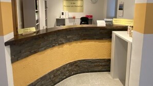 Un área de recepción con mostrador de piedra, un reloj en la pared y un cartel de bienvenida.