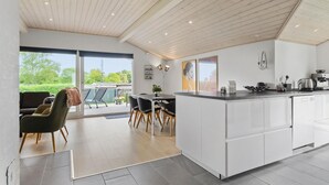 A modern kitchen with white cabinets, a central island, and a dining area with chairs and a table. - 3 bedroom stunning home in Hejls (Hejls)