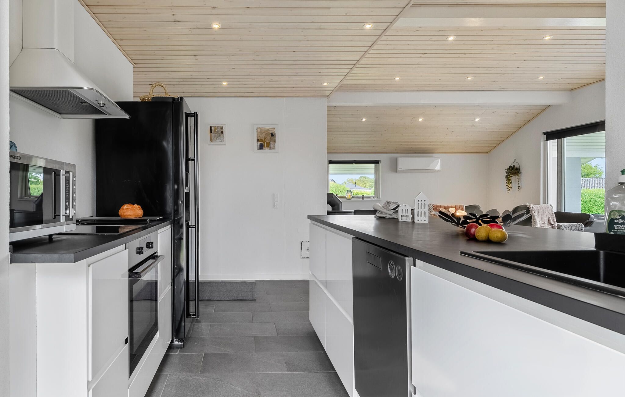 A modern kitchen with a black refrigerator, a microwave, and a stove. There is a window with a view of greenery outside.