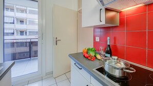 A modern kitchen with red tiles, a stove, and a variety of fresh vegetables on the counter.