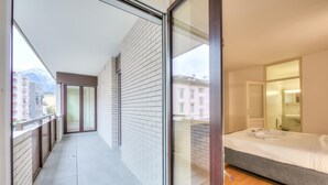 A modern hotel room with a balcony, a bed, and a bathroom visible through a glass door.